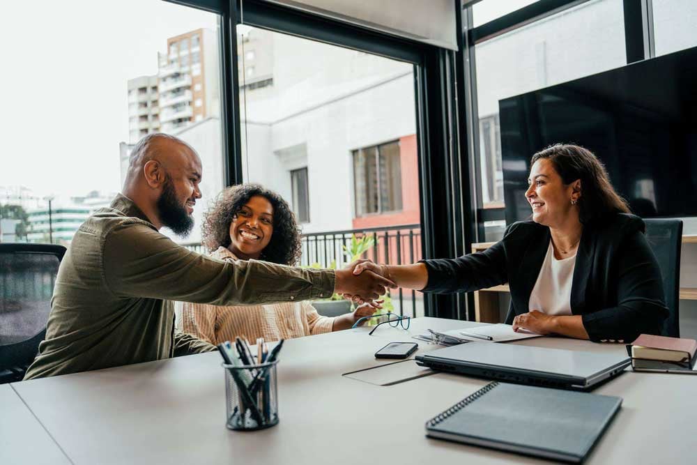 A young smiling couple sit in a conference room and shake hands with an insurance agent.