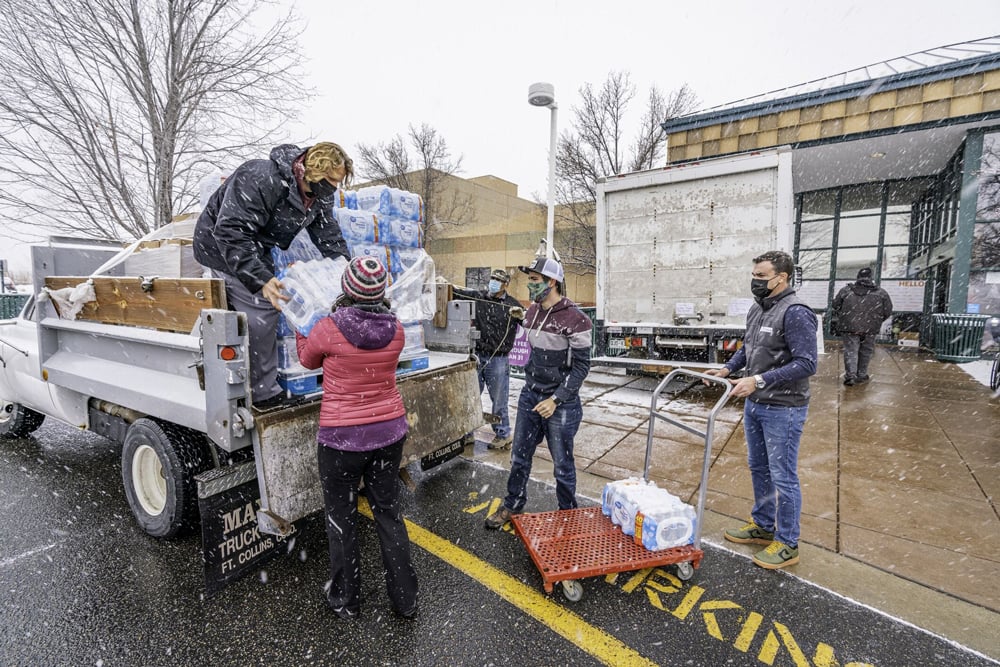 Relief volunteers unload packages of bottled water from the back of a truck in the snow, loading it onto a trolley to take into a community center.