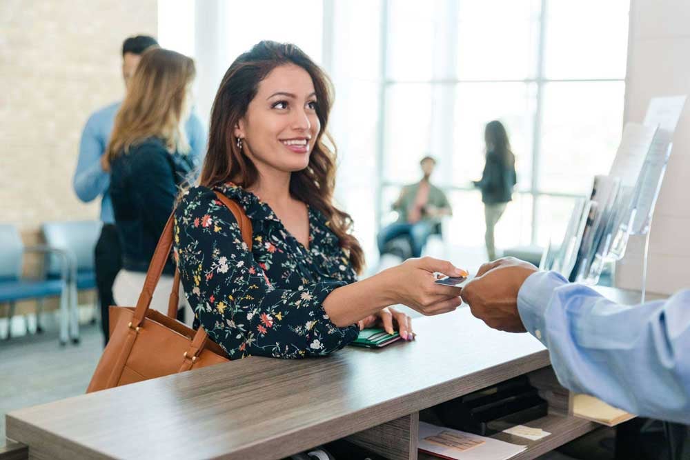 A smiling young woman hands her debit card to an off-camera bank teller so she can make a deposit into her bank account.