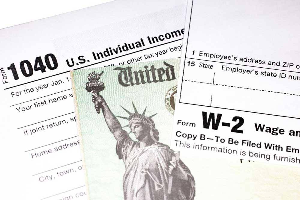 A close-up of multiple documents, including a 1040 tax form, a W-2 wage statement, and a tax refund check.