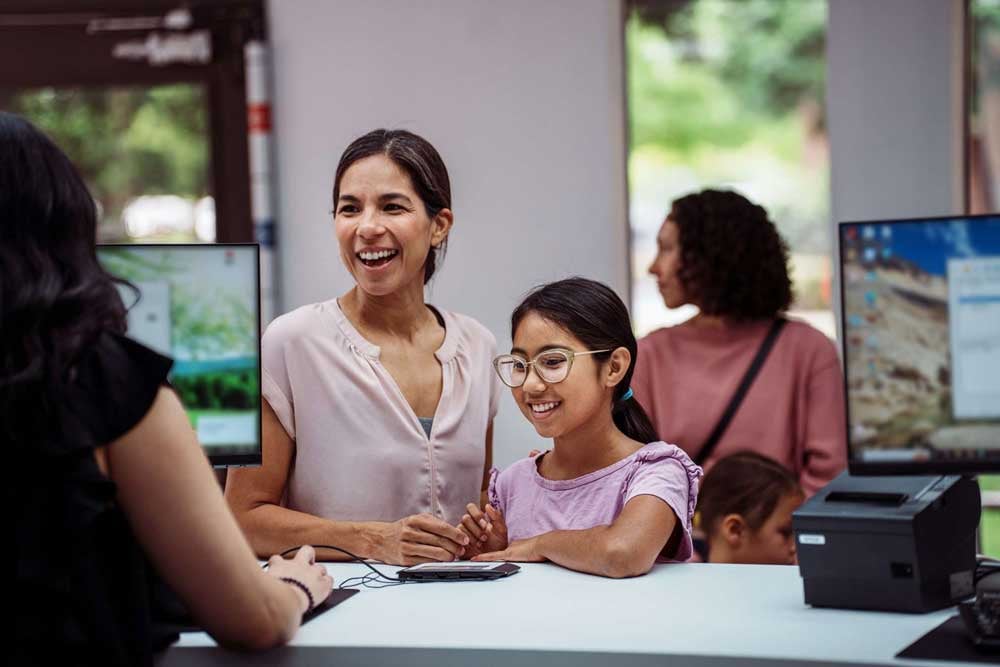 A preteen girl of Latin American descent smiles with pride and excitement while opening a savings account at a credit union, accompanied by her mother.