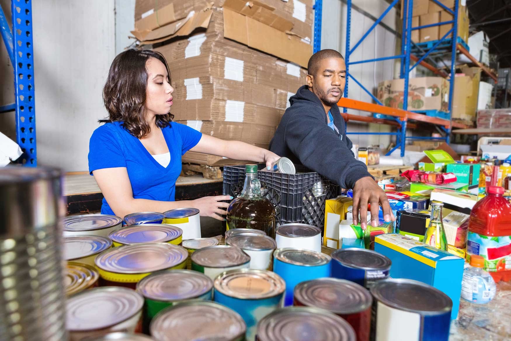 A young woman and young man work together to sort food donations for a charity organization. 