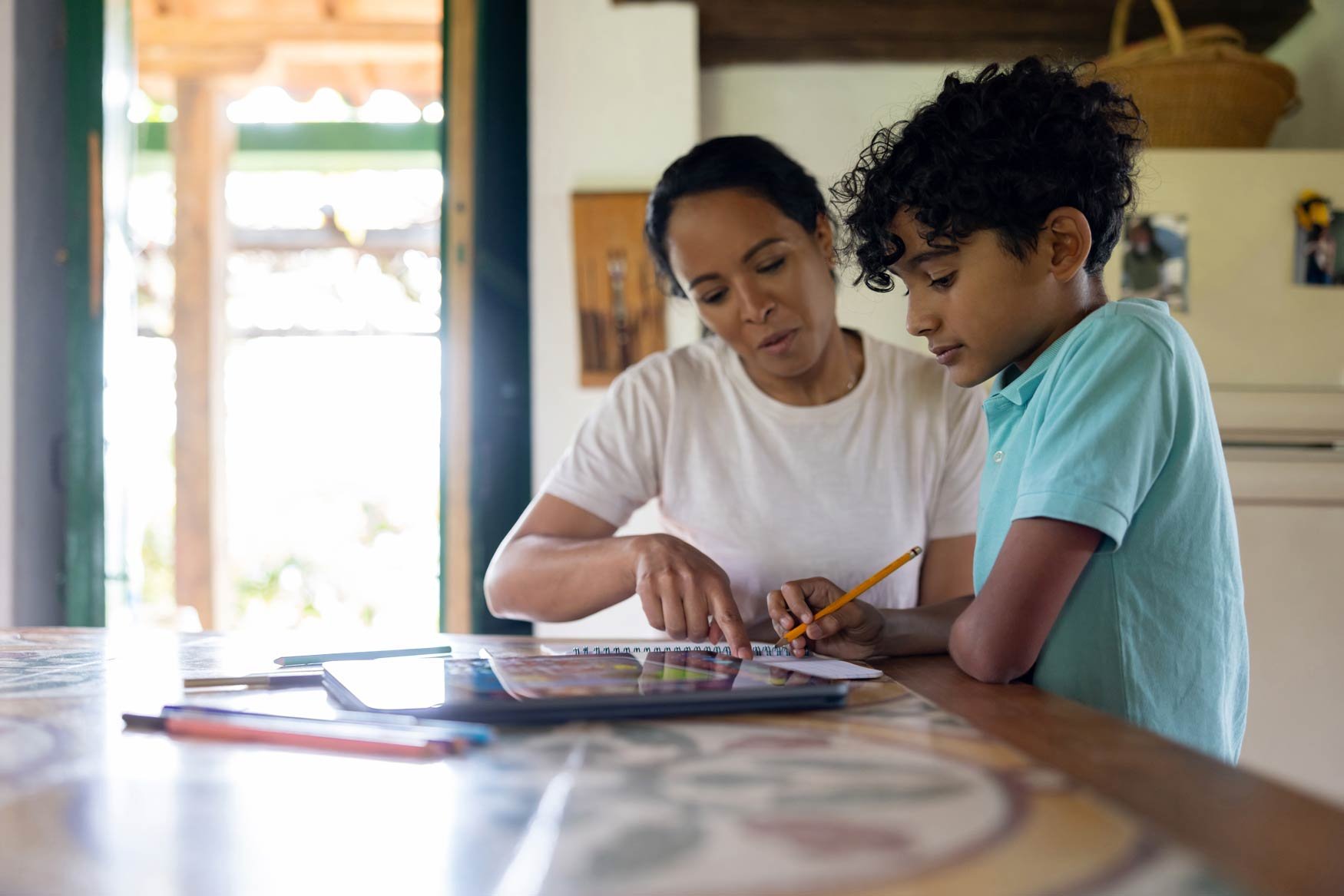 A mother sits at a table with her young son, helping him with his homework. 