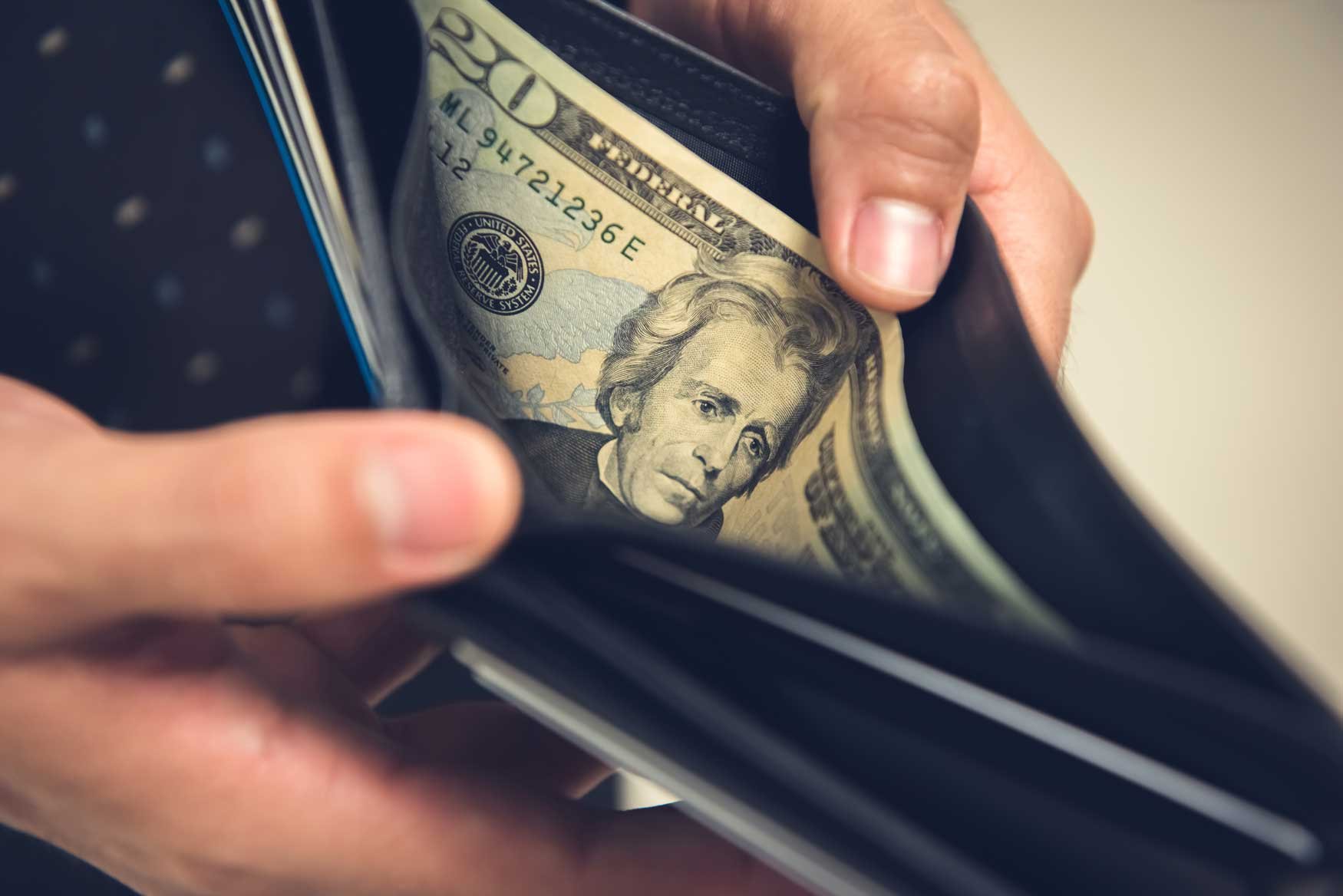 A closeup of two hands holding open a wallet with a twenty dollar bill inside. 