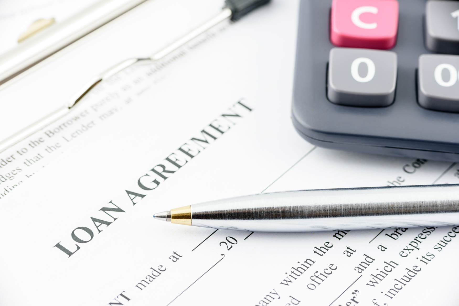 A closeup of a calculator and pen sitting on top of paperwork with the words Loan Agreement at the top.