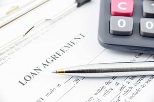 A closeup of a stack of papers with a calculator and a ballpoint pen on top. At the top of the page it says, “Loan Agreement.”