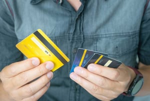 A close-up photo of a man’s hands, holding several credit and debit cards, trying to choose which to use. 