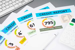 A closeup on a series of papers splayed on a desk, each depicting a credit report with different scores.