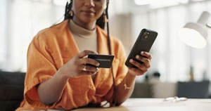  A photo focusing on the hands of a young woman holding a credit card and her smart phone while the rest of her body is blurred in the background. 