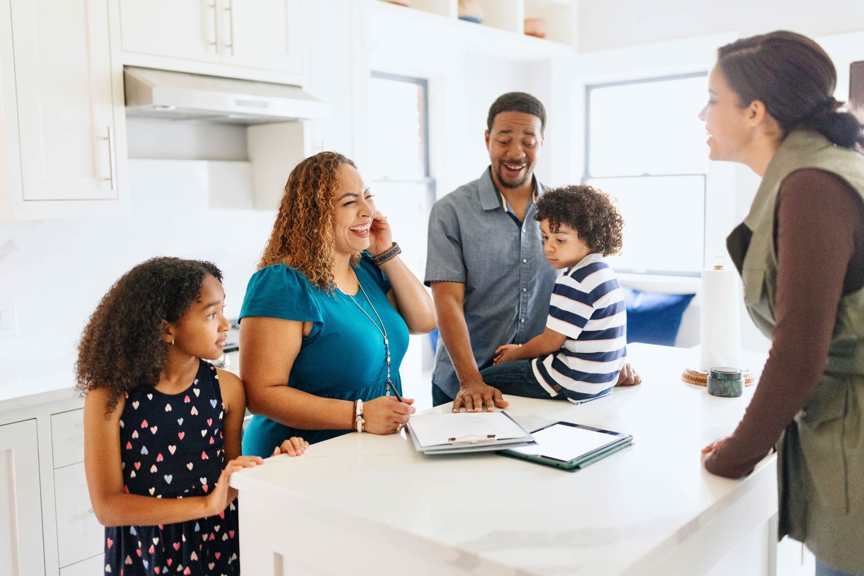 A happy family with two young children stand in a kitchen with a young woman as they fill out paperwork.
